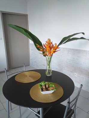 A round dining table with two placemats, a vase with flowers, and a bowl of food. - A corner of greenery .. (St Joseph)