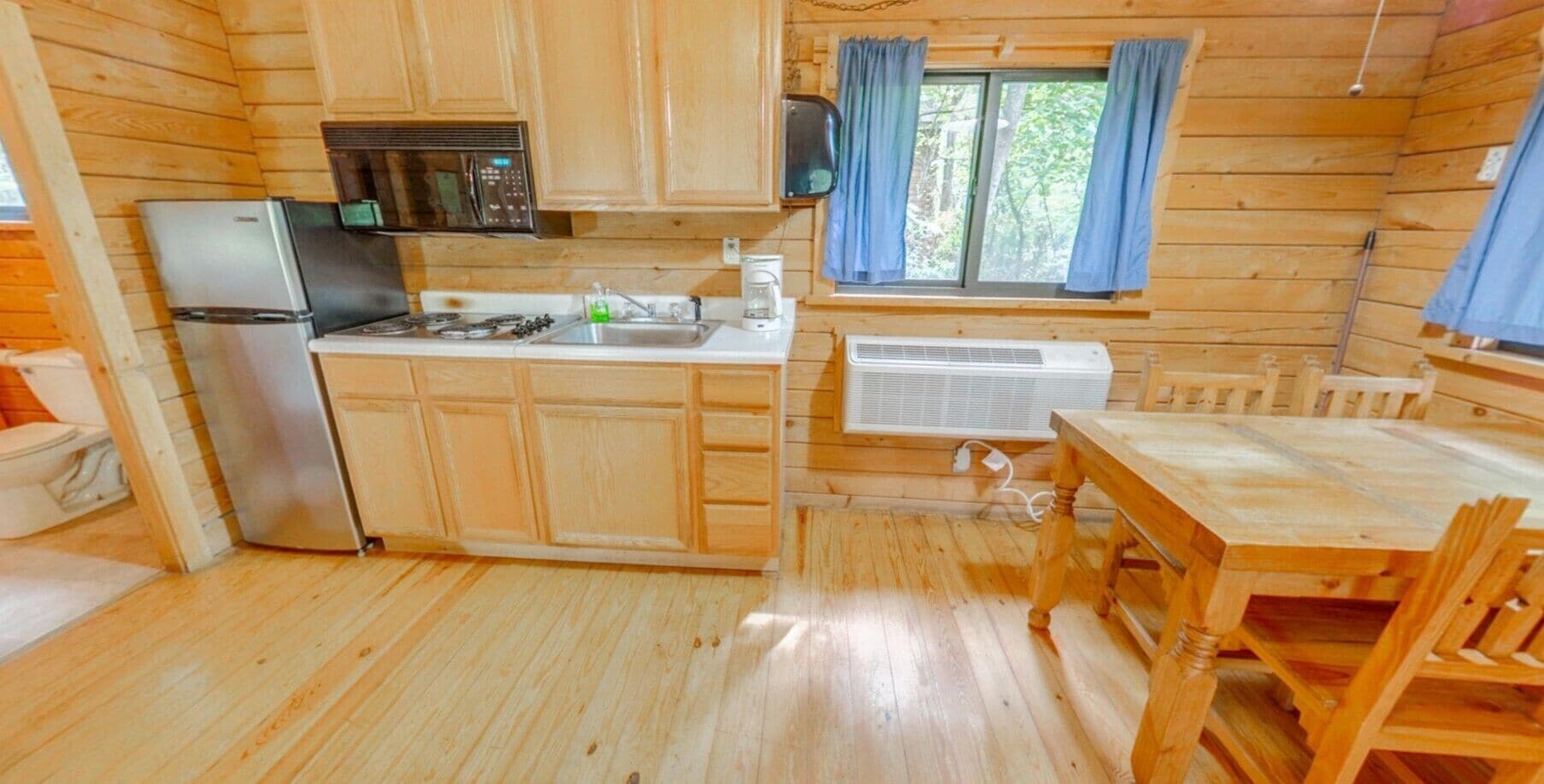 Una baita in legno con una cucina accessoriata, dotata di frigorifero, fornello, microonde e una finestra con tende.