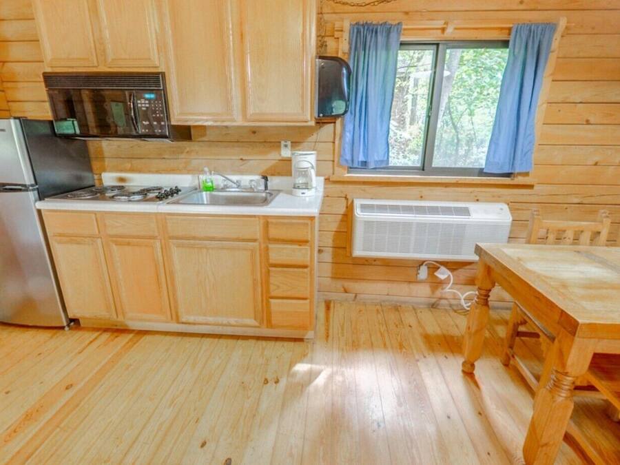 Una baita in legno con una cucina accessoriata, dotata di frigorifero, fornello, microonde e una finestra con tende.