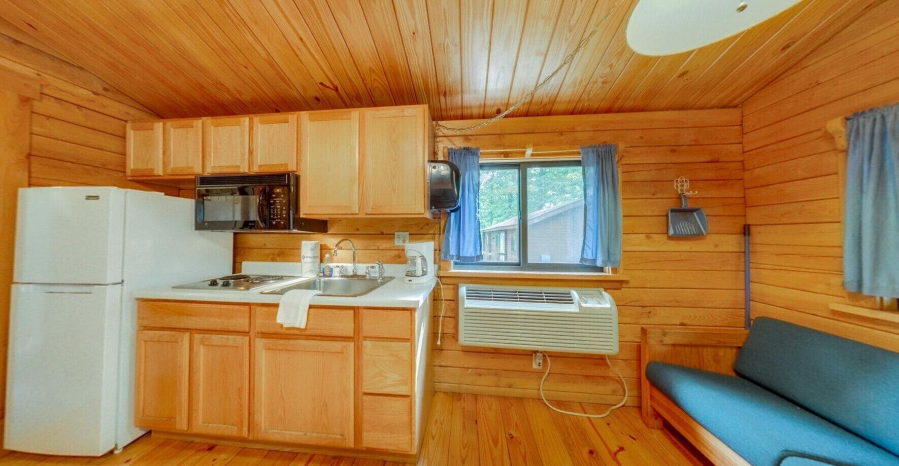 A cabin-style kitchen with wooden cabinets, a refrigerator, a microwave, and a window with curtains.