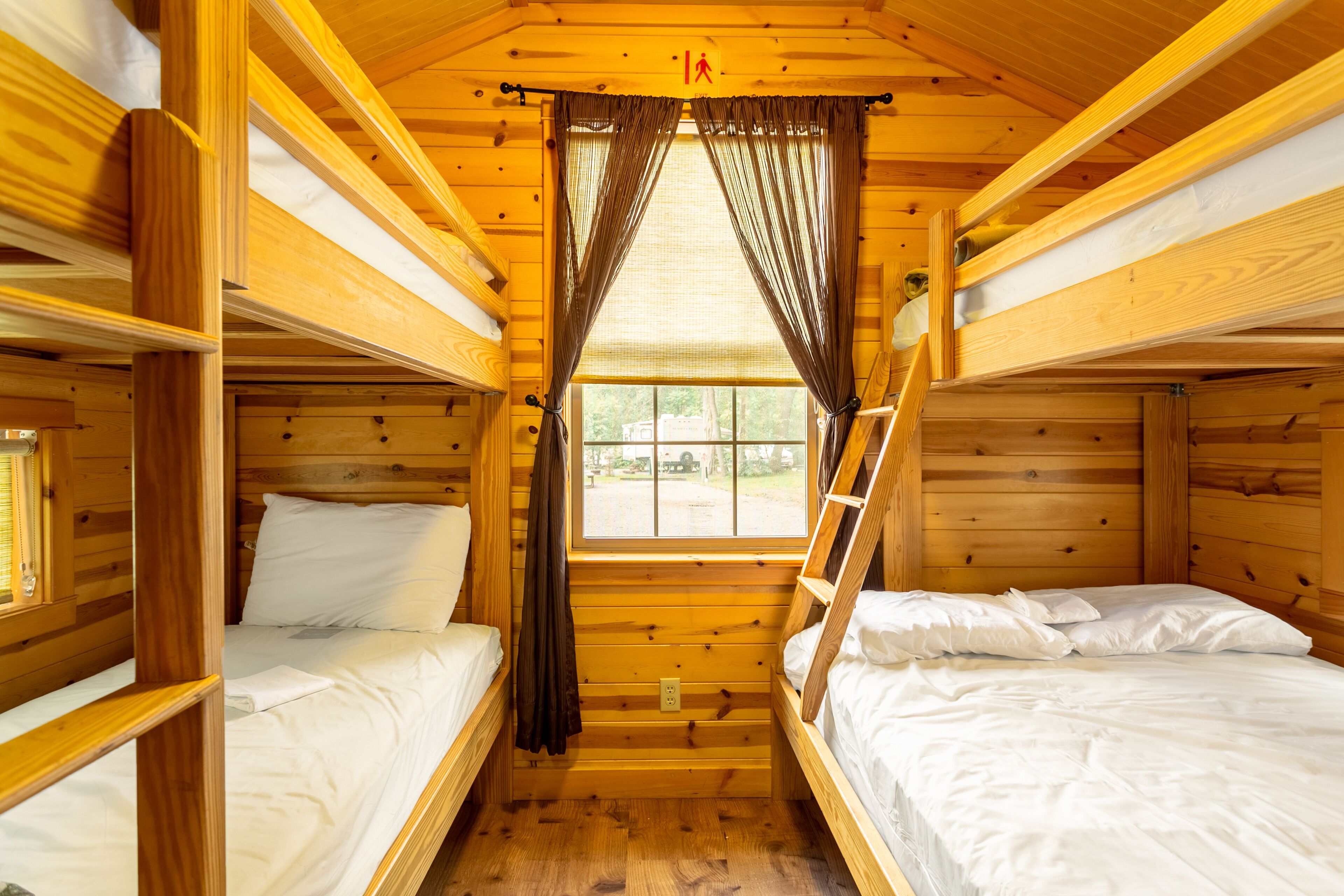 Eine Holzhütte mit Etagenbetten, einem Fenster mit Vorhängen und einem sichtbaren Fluchtweg.