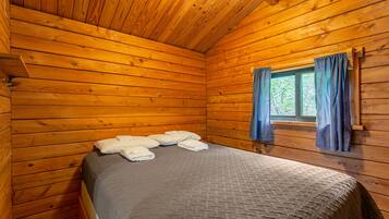 A wooden cabin room with a bed, a window with curtains, and a wooden ceiling.