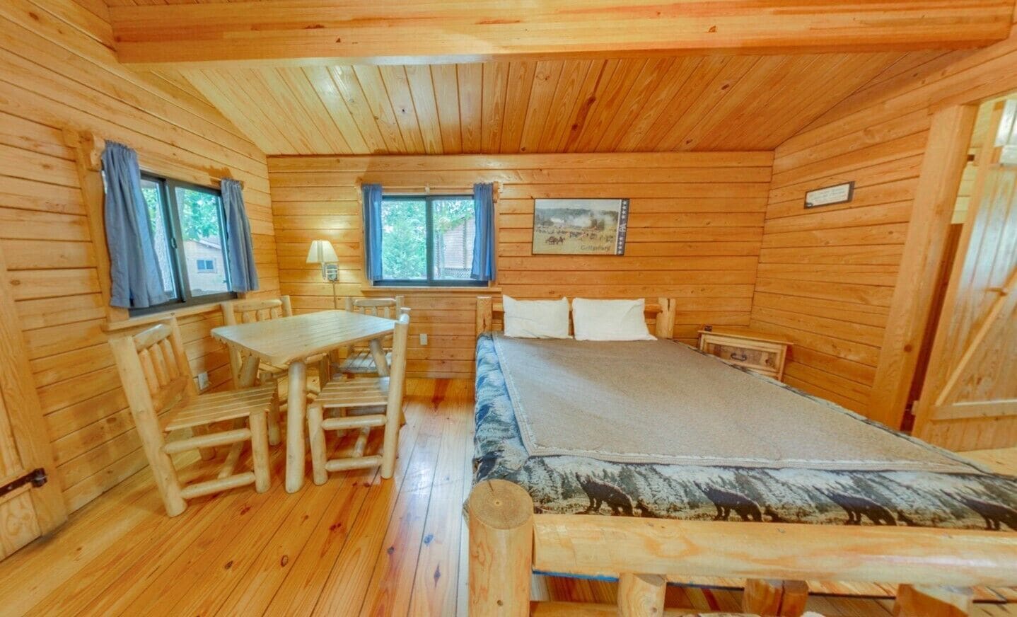 Habitació d'una cabana de fusta amb un llit, una taula i dues cadires.