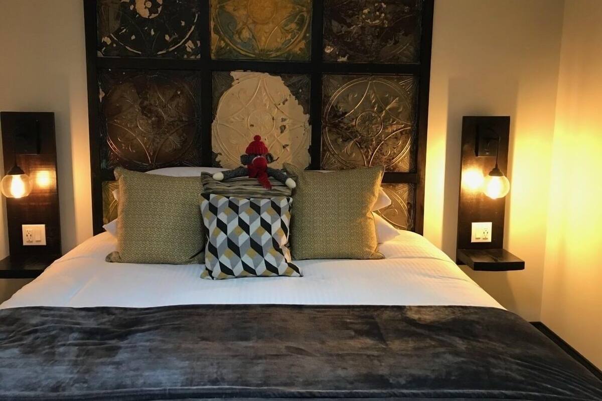 A neatly made bed with a geometric patterned pillow, a plush blanket, and a decorative item on the headboard.
