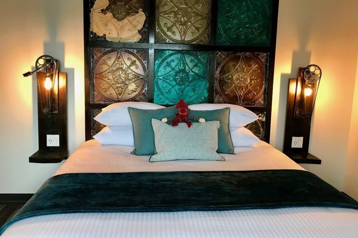 A neatly made bed with a dark blanket, multiple pillows, and a decorative red ornament.