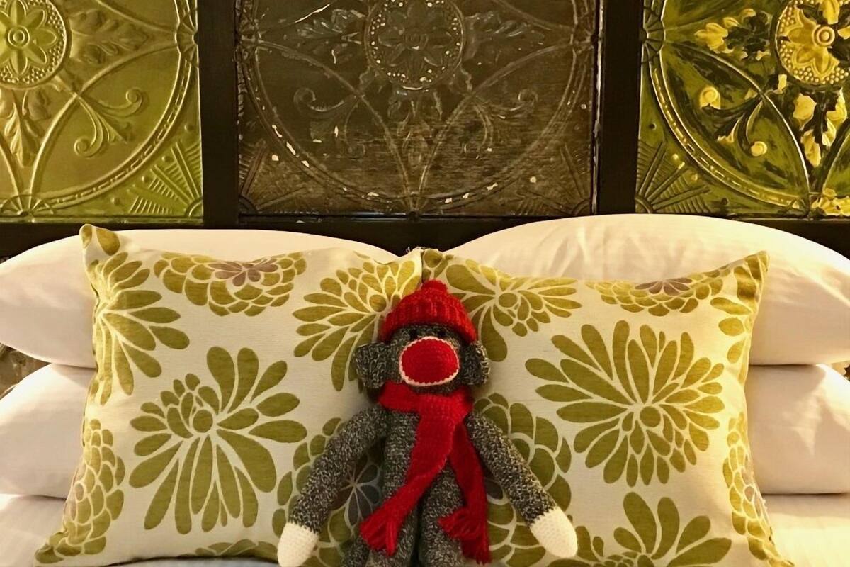 A pillow with a monkey figure and a red scarf on a bed with a floral patterned pillowcase.