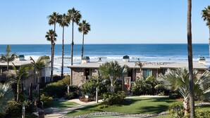 A beachfront hotel with multiple-story buildings, palm trees, and a clear view of the ocean.
