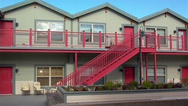 A two-story building with a red staircase leading to a balcony, outdoor seating, and a small garden area.