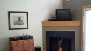 A living room with a fireplace, a television on a wooden shelf, a framed picture on the wall, and a cabinet.