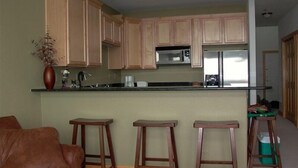 A modern kitchen with wooden cabinets, a stainless steel refrigerator, and a bar stool.