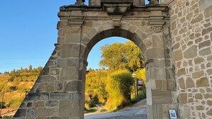 An arched stone gateway with a statue on top, leading to a building with a stone facade. - Casa Rural Osante (Labastida)