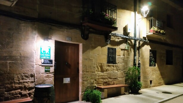 A stone building with a wooden door, a sign for a restaurant, and a bench outside. - Casa Rural Osante (Labastida)