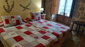 A bedroom with two beds, a stone wall, a window with a view, and a small table. - Casa Rural Osante (Labastida)