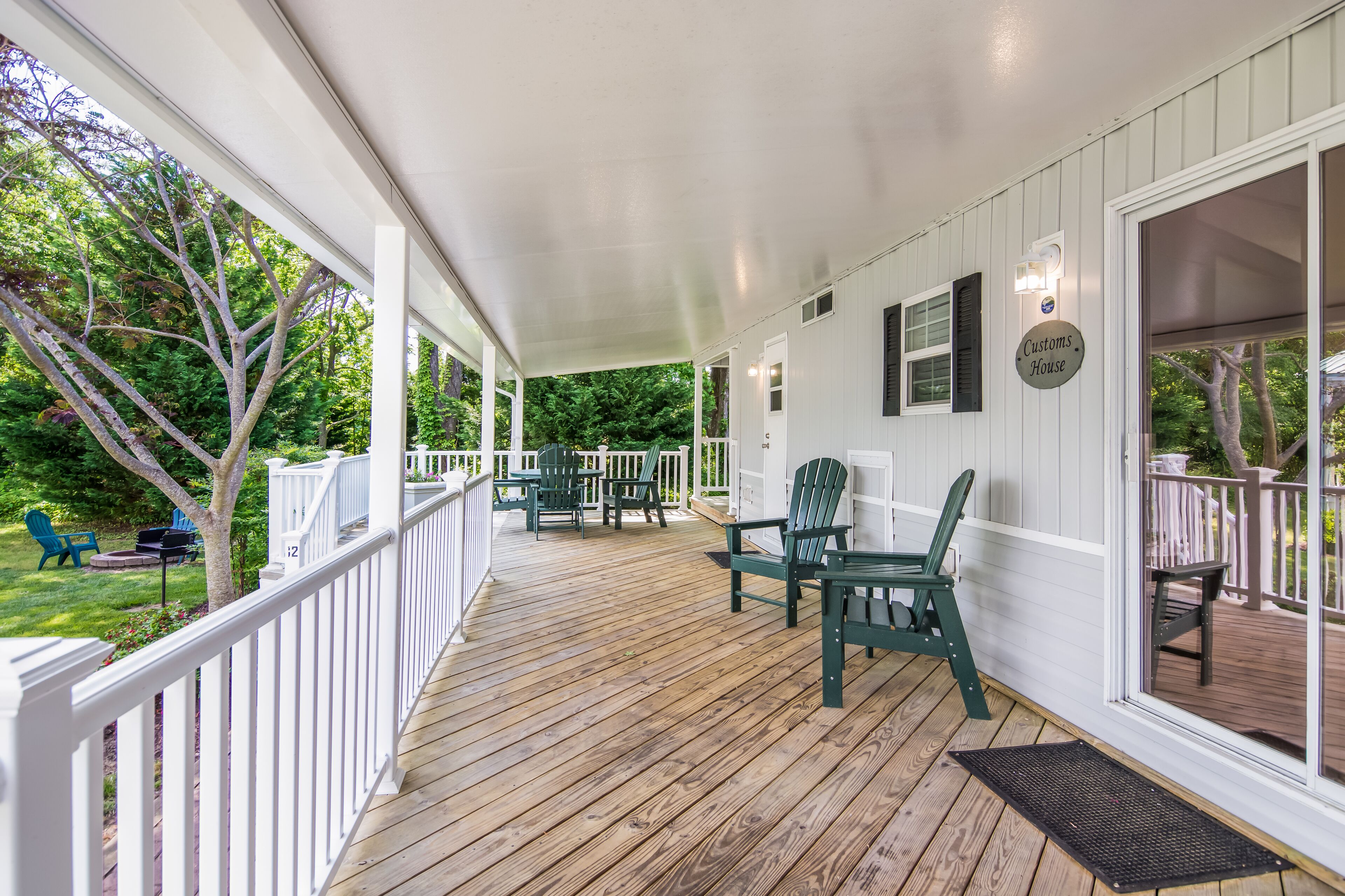 A covered porch with wooden flooring, white railings, and green Adirondack chairs.
