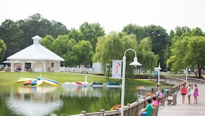A wooden boardwalk beside a calm lake with a gazebo and paddle boats. - Bethpage Camp-Resort (Urbanna)