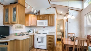 A compact kitchen with wooden cabinets, a microwave, a stove, and a dining area with chairs and a table. - Bethpage Camp-Resort (Urbanna)