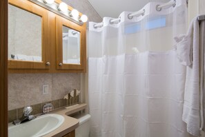 A bathroom with a sink, two mirrors, a shower curtain, and a towel rack. - Bethpage Camp-Resort (Urbanna)