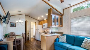 A compact kitchen with wooden cabinets, a microwave, and a sink. There is a dining table with chairs and a blue sofa with patterned cushions. - Bethpage Camp-Resort (Urbanna)