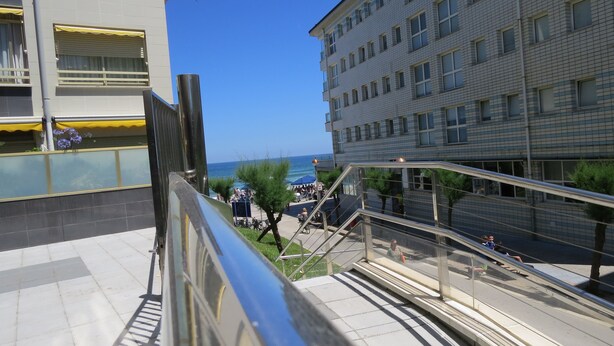 A view from a balcony overlooking a coastal area with a clear sky, a pedestrian walkway, and a building with a tiled facade. - Front line with sea views garage + free wifi (Zarauz)