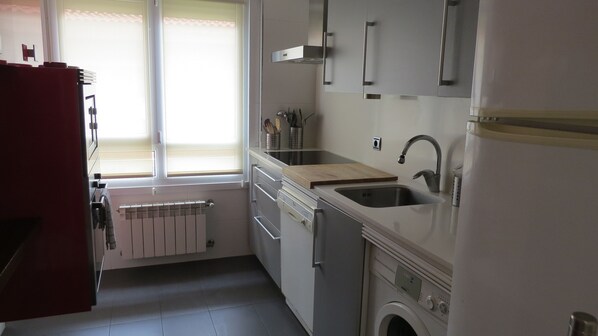 A compact kitchen with a built-in washing machine, a sink, and a window with blinds. - Front line with sea views garage + free wifi (Zarauz)