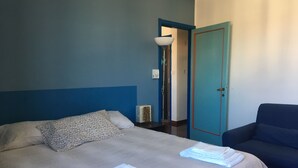 A bedroom with a bed, a blue chair, and a door. - Casa Arcobaleno, an experience to try! (Firenze)