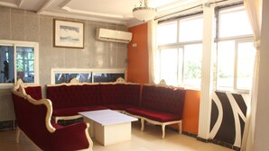 A living room with a red sofa, a white coffee table, and a large window with curtains. - Complexe Hotelier St Elie (Yaoundé)