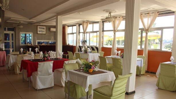 A restaurant with multiple tables, each set with white tablecloths and green chairs. - Complexe Hotelier St Elie (Yaoundé)