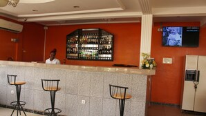 A bar area with a counter, three stools, a refrigerator, and a television mounted on the wall. - Complexe Hotelier St Elie (Yaoundé)