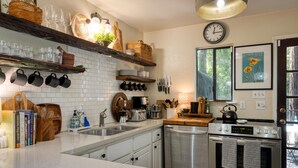 Una cocina moderna con baldosas blancas, electrodomésticos de acero inoxidable y estantes de madera.