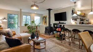 Una sala de estar acogedora con chimenea, televisor y una zona de cocina con taburetes de bar.