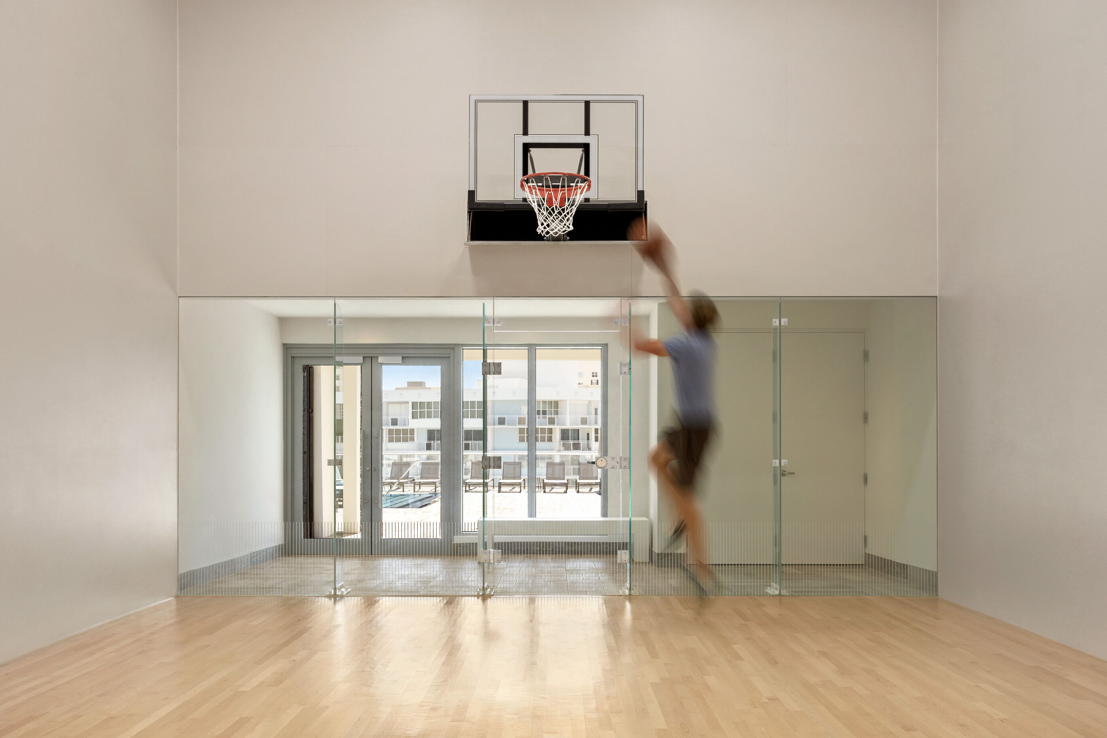 A basketball hoop in a modern indoor space with a glass partition and a bench.