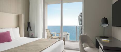 Ein Hotelzimmer mit Bett, Schreibtisch, Stuhl, Lampe und Blick auf das Meer und die Stadt.