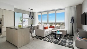 A modern hotel room with a kitchen area, a sofa set, a dining table, and a large window offering a city view. - Hyde Beach House (Hollywood)