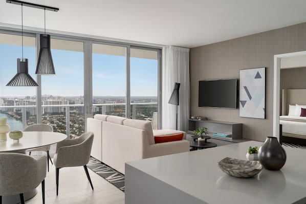 Una habitación de hotel moderna con un balcón grande, un televisor de pantalla plana, un sofá, una mesa de comedor y una decoración minimalista.