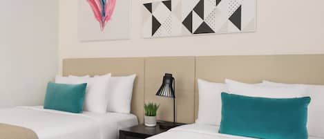 A hotel room with two beds, white bedding, teal pillows, a small potted plant, and abstract wall art.