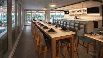 Una larga mesa de comedor con varias sillas, un área de bar con televisor y ventanas amplias que dan a vistas del exterior.
