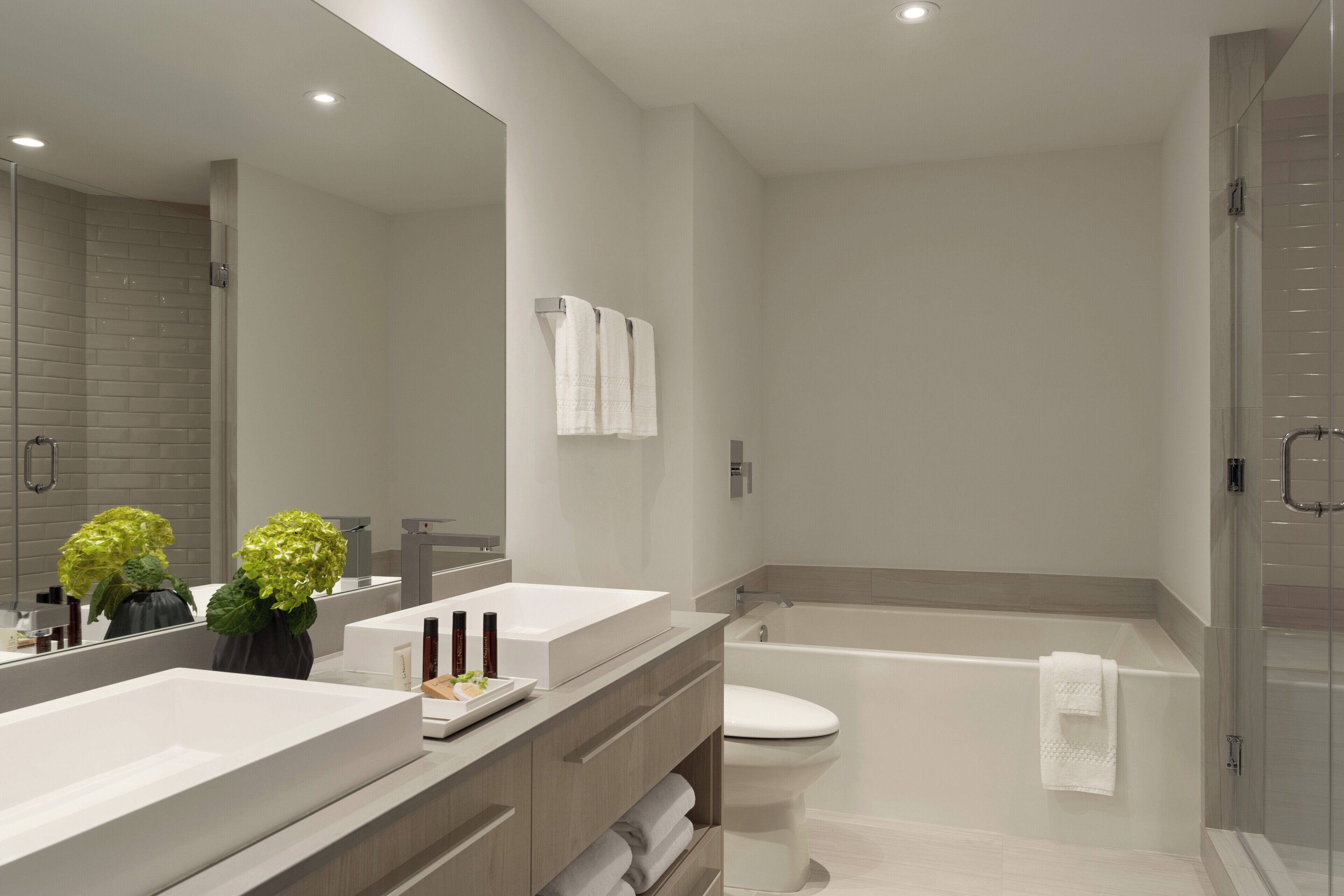 Un baño moderno con un espejo grande, dos lavamanos, un inodoro y una bañera.