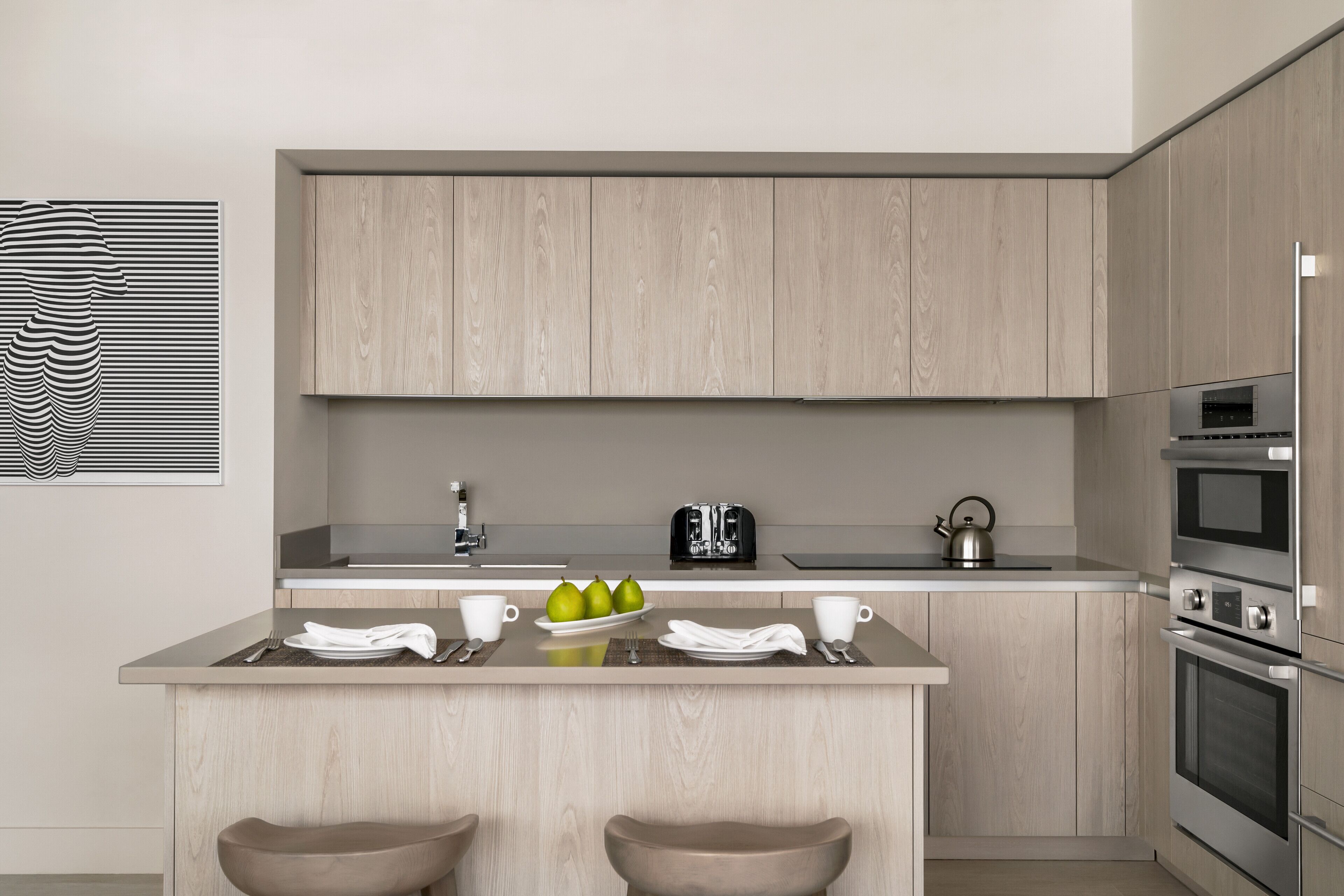 A modern kitchen with wooden cabinets, a central island with stools, a kettle, and a toaster.