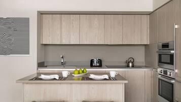 A modern kitchen with wooden cabinets, a central island with stools, a kettle, and a toaster.