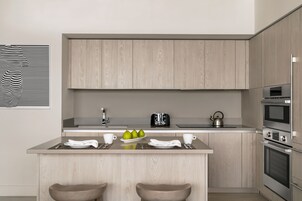 A modern kitchen with wooden cabinets, a central island with stools, a kettle, and a toaster.