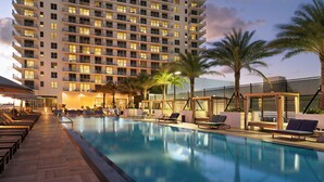 A hotel pool area with lounge chairs and palm trees, surrounded by a high-rise building. - Hyde Beach House (Hollywood)