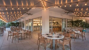 An outdoor dining area with round tables and wooden chairs, ceiling fans, and string lights. - Hyde Beach House (Hollywood)