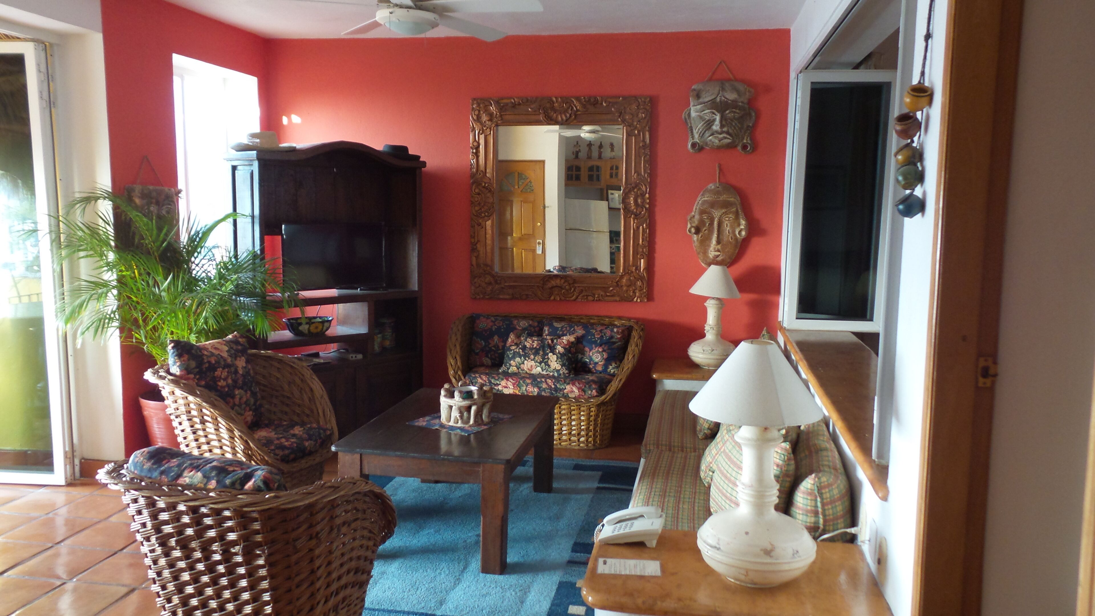 Una sala de estar con pared roja, un espejo grande, un sofá, una mesa de centro y un televisor.