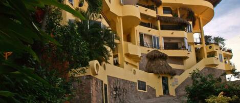 Un edificio de varios pisos con fachada amarilla, balcones y techo de paja.