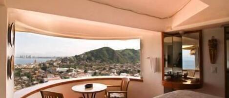 A hotel room with a balcony, a bed, a small table, and chairs.