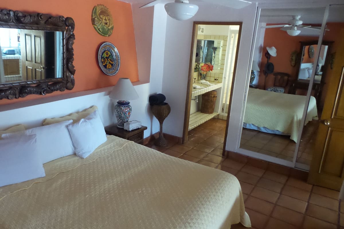 A bedroom with a large bed, a mirror, decorative plates, a lamp, and a door leading to another room.