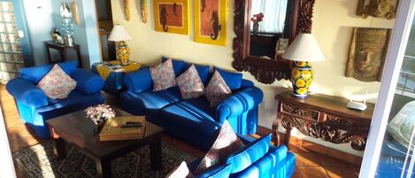 Een woonkamer met blauwe banken, gestreepte kussens, een salontafel en decoratieve items aan de wanden.