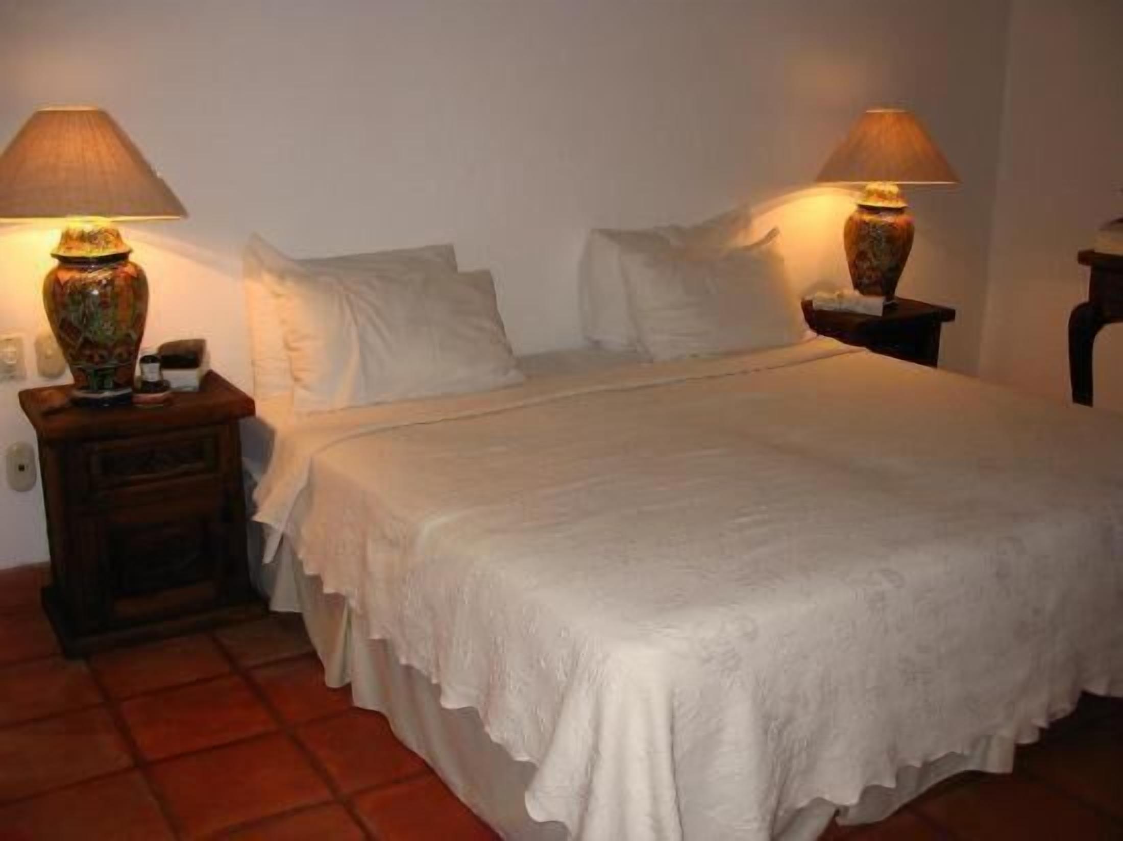 A neatly made bed with a white bedspread and pillows, flanked by two nightstands with lamps.