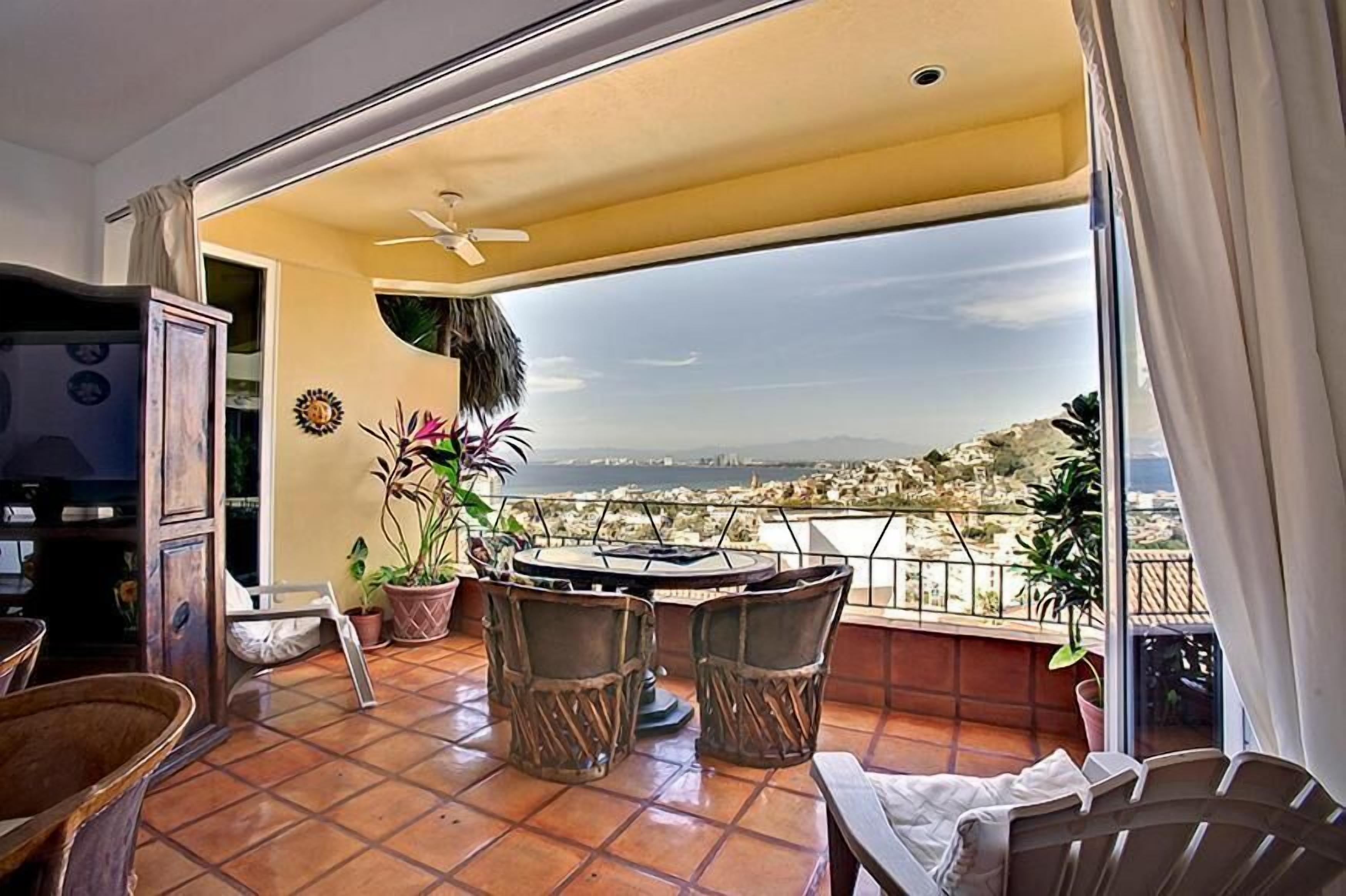 A balcony with a table and chairs, potted plants, and a view of a cityscape.