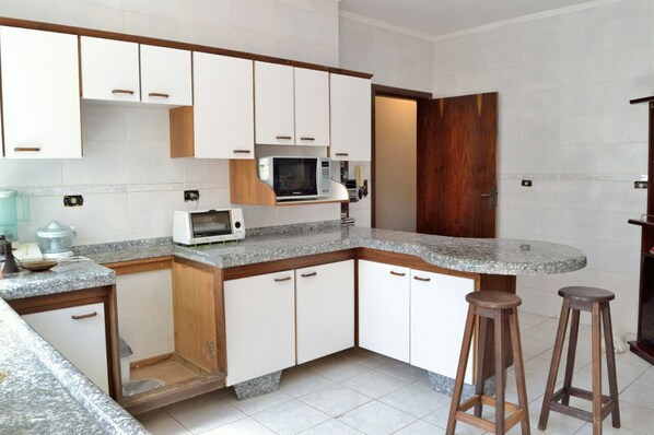 A kitchen with white cabinets, a microwave, a toaster, and two stools.